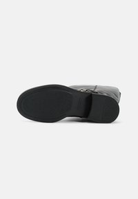 Bota de tornozelo em couro preto com sola de borracha texturizada, apresentando um fecho lateral e um detalhe de costura mínima. A vista inferior mostra o padrão da sola.