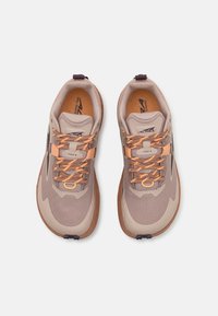 Baskets de course beige avec tige en mesh, accents texturés et lacets orange. Elles disposent d'une semelle rembourrée et d'une languette de talon à boucle pour un enfilage facile.