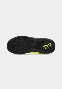 Zwart atletisch schoenzool met gestructureerd rubber voor grip, met felle gele accenten en een "TYR"-logo nabij de hak.