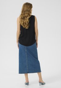 Haut sans manches noir associé à une longue jupe en denim bleu et des mules à talons bleu clair. Tissu lisse et forme structurée avec une fente dans le dos.