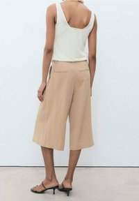 Culottes beiges à coupe large, confectionnées dans un matériau léger. Elles présentent deux poches arrière et sont associées à un haut blanc sans manches.