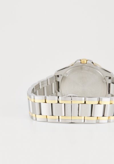 Orologio in acciaio inossidabile argentato con accenti in oro giallo. Presenta un bracciale in metallo, maglie testurizzate e una cassa rotonda con un retro dettagliato.