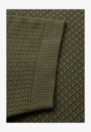 Tissu tricoté texturé en vert olive foncé, avec un motif en grille et des accents côtelés le long des bords, créant une profondeur de surface variable.