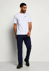 Světle šedé tričko s krátkým rukávem a malým černým logem, spárované s tmavě modrými kalhotami. Černá obuv dotváří outfit.