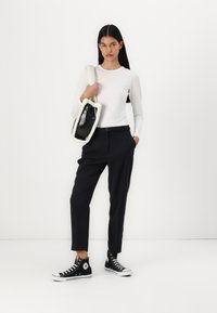 Haut à manches longues blanc, pantalon ajusté bleu marine et baskets montantes noires. Sac à main noir avec une bandoulière blanche en fourrure. Design minimaliste.