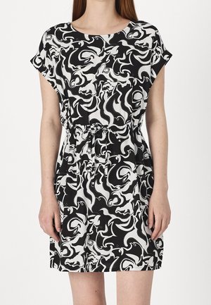 Femme portant une robe à manches courtes à motif abstrait noir et blanc, avec un col rond et une taille cintrée.
