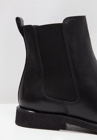 Bottine noire en cuir avec panneau latéral élastique et languette, dotée d'une semelle basse texturée et de coutures détaillées.