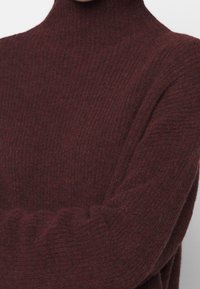 Burgundy-coloured turtleneck neulepaita, joka on valmistettu ribbikuvioidusta kankaasta ja joka on muotoon ommeltu sekä pehmeä. Pidennetyt hihat ja minimaalinen yksityiskohtaisuus.