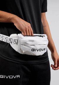 Mano nella tasca con zip di una borsa a vita bianca GIVOVA indossata sopra abbigliamento sportivo nero GIVOVA all'anca di una persona.