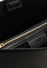 Zwarte leren tasinterieur met een gouden ritszak en een reliëf "MNG" logo op een leren label binnenin de tas.