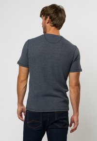 Camiseta de manga corta gris oscuro con un patrón de tejido texturizado, escote redondo y sutilezas en los detalles de costura, combinada con unos vaqueros azul oscuro.