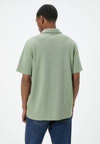Groene getextureerde poloshirt met korte mouwen en een klassieke kraag, gecombineerd met blauwe denim jeans.