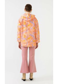 Multifarvet hættetrøje med abstrakt blomstermønster i orange, pink og lilla. Kombineret med vide pink bukser og beige støvler.