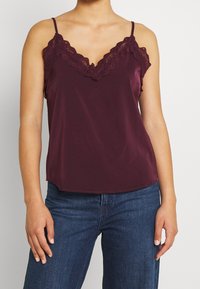 Camisola in satin bordeaux con pizzo, dotata di spalline regolabili, scollatura a V e orlo leggermente curvo.