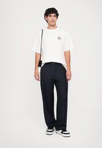 Hvit oversized t-skjorte med logo, paret med marineblå stripete bukser. Brukt med svart og hvit sneakers, og en liten svart crossbody-veske.
