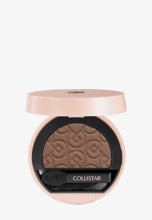 Petit boîtier rond beige d'ombre à paupières ouvert révélant une ombre à paupières pressée marron avec un motif embossé et un petit pinceau noir portant l'étiquette "Collistar".