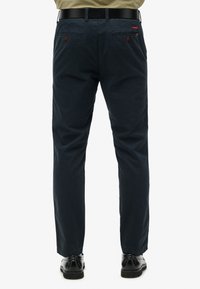 Navyblauwe trousers van katoen met een gladde textuur. Voorzien van achterzakken met bruine knopen en een zwarte riem. Klassiek recht model.