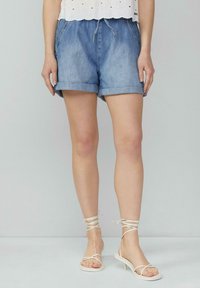 Shorts en denim avec des ourlets roulés, couleur bleu clair, taille élastique avec cordon de serrage. Associés à des sandales blanches à lanières.