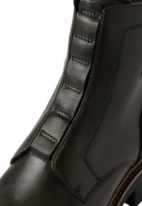 Bottine en cuir noir avec panneaux latéraux élastiques, surface texturée, finition lisse, couture renforcée et semelle marron contrastante.