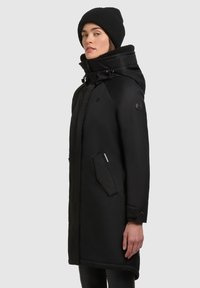 Parka neagră izolată cu glugă, dotată cu un buzunar cu fermoar, manșete cu dantelă și o căptușeală moale. Design curat și elegant, cu un fermoar frontal.