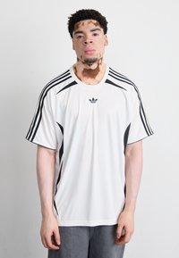 White athletic shirt with black side accents and three black stripes on each shoulder. Lightweight fabric, crew neck design.