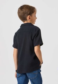 Sort kortærmet skjorte i tekstureret stof med krave, rygstykke og lige kant, kombineret med blå denimjeans.