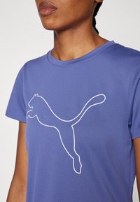 T-shirt atlético roxo com mangas curtas e decote redondo, apresentando um contorno branco de um logotipo de puma a saltar na frente. Textura suave.