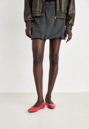 Gonna a righe bianche e nere, con elastico in vita, abbinata a scarpe basse rosse. Stilizzata con un giubbotto bomber verde oliva. Tessuto liscio.