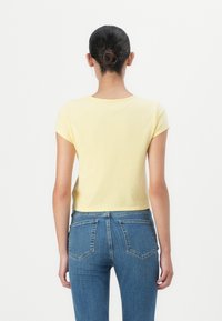 Yellow short-sleeve T-shirt with a round neckline, paired with mid-rise blue denim jeans featuring back pockets and a fitted silhouette.