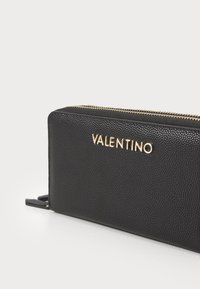 Black textured leather wallet with gold hardware; features the brand name "VALENTINO" embossed on the front, zip closure, and side accents.