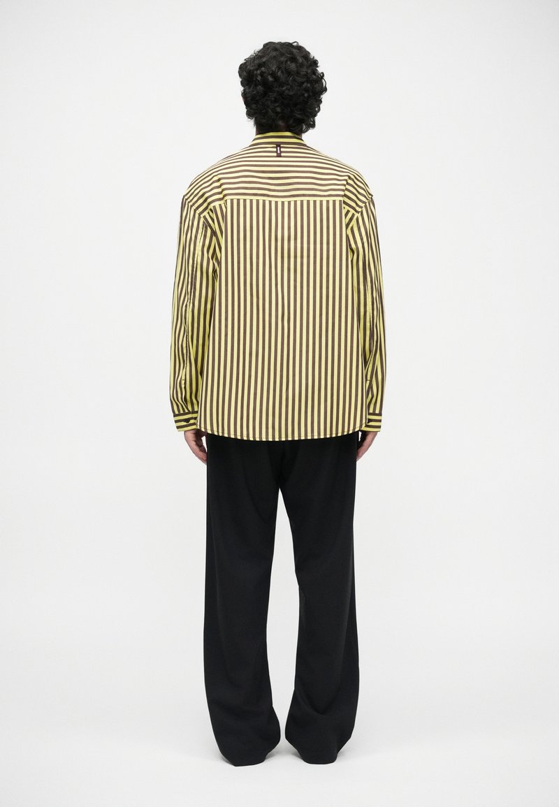Striped shirt in yellow and brown fabric with a collar, long sleeves, and a straight cut, paired with loose black trousers.