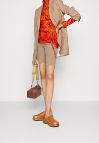 Beige blazer, färgglad mönstrad turtleneck, ribbade beigefärgade shorts och bruna plattformsträskor. Håller en liten brun väska med en avtagbar rem.