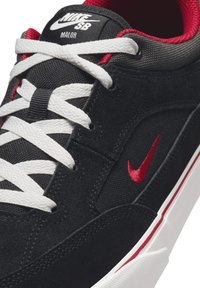 Čierne semišové tenisky s bielymi šnúrkami, červenými akcentmi a bielou podrážkou. Obsahuje logo na jazyku a boku, s textúrovaným detailom tkaniny.