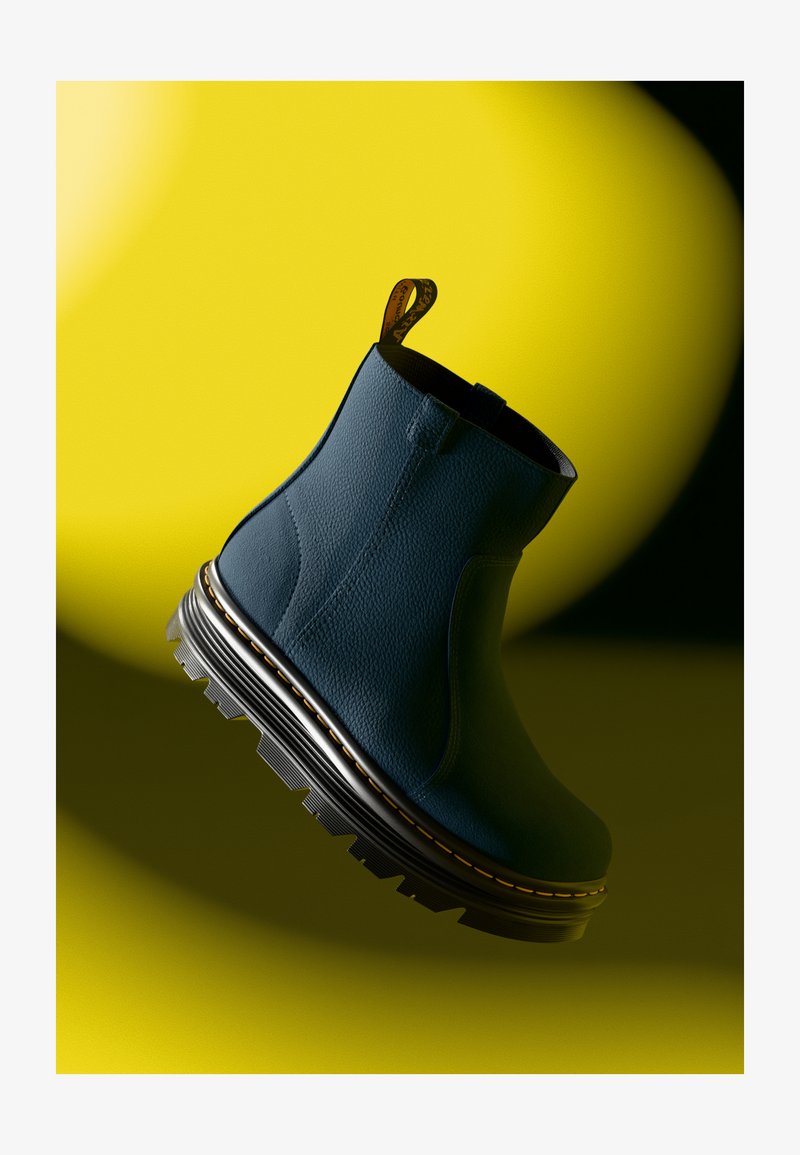 Bottine bleue en cuir avec surface texturée, semelle en caoutchouc noir épais et couture jaune, équipée d'une languette à l'arrière.