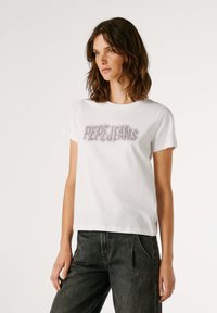 Camiseta de algodón blanca con mangas cortas y cuello redondo, que presenta el nombre de la marca "PEPE JEANS" en strass en el pecho. Ajuste casual.