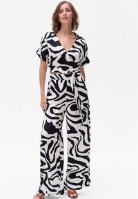 Zwart-witte wikkeljumpsuit met brede benen, korte mouwen, abstract patroon en een gestrikte taille. Glad stof met een vloeiende val.