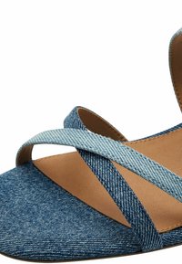 Denim-wedge-sandaalit, joissa on ristikkäiset hihnat ja sileä ruskea pohja. Sininen denim, jossa on hienovarainen rakenne ja avonainen varvasmuoto.