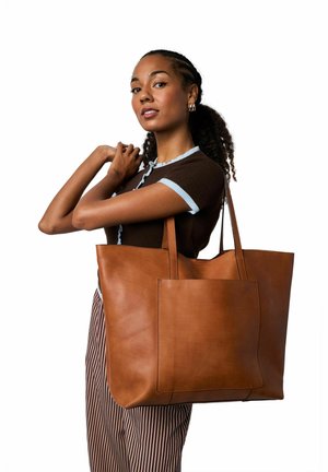 Brun læder shoppertaske med to lange håndtag, har en frontlomme, glat tekstur og en struktureret rektangulær form.