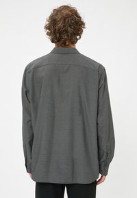 Chemise à manches longues en tissu gris foncé avec un motif à carreaux subtil, dotée d'un empiècement dans le dos, de poignets à boutons et d'une coupe décontractée.