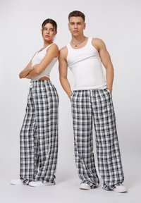 Pantaloni da lounge a quadri in bianco e nero con vestibilità ampia e cintura elastica. Abbinati a top bianchi senza maniche e sneaker, design minimalista.