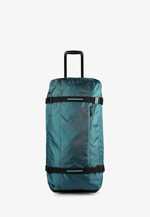Sac de voyage à roulettes bleu sarcelle avec poignée noire extensible, deux sangles latérales réglables et une poche avant zippée, debout sur un fond blanc.