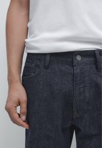 Dark denim jeans made of cotton with a smooth texture, featuring a button closure, belt loops, and a classic five-pocket design.