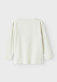 Top de algodón blanco de manga larga con cuello redondo y corte relajado. La tela tiene una textura suave, con costuras simples en los dobladillos.