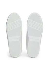 Le suole delle sneaker bianche in gomma presentano un motivo testurizzato per una buona aderenza, con un marchio in rilievo. Il design è semplice e piatto.