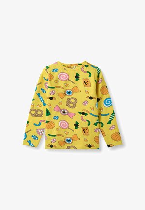 Žuta košulja dugih rukava s racionalnim uzorkom slatkiša koji sadrži različite oblike, uključujući lizalice, crve i perece. Pamuk.