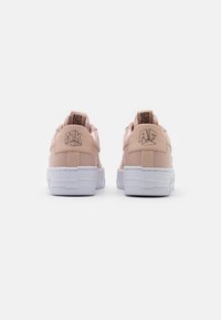 Ljust rosa sneakers med vita sulor, med präglad branding "NK" och "AF" på hälarna och en slät läderliknande textur.