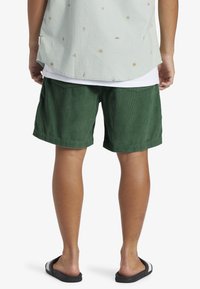 Pantaloni corti in corduroy verde con una vestibilità comoda, caratterizzati da un orlo risvoltato e tasche posteriori cucite, abbinati a sandali neri a scivolo.