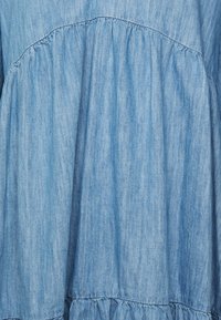 Tessuto di denim azzurro chiaro con un design arricciato e volant all'orlo e al corpetto. Texture morbida con sottili righe verticali.