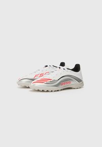 White soccer cleats with black and red accents, featuring a silver side panel. Includes a textured outsole and lace-up design. "MESSI" logo displayed.