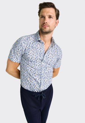 Kurzärmeliges Hemd mit Knöpfen und einem hellblauen Blumenmuster, aus Baumwolle gefertigt. Kombiniert mit dunkelblauen Hosen mit Kordelzugbund.